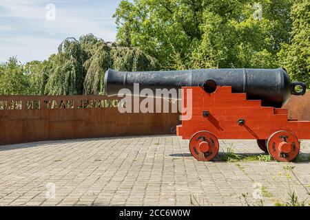 Alte schwarze Feuerkanone auf einem orangefarbenen Holzsockel auf dem Rondeel (De Vijf Koppen) mit grünen Bäumen im Hintergrund, alte Maastricht-Stadt Stockfoto