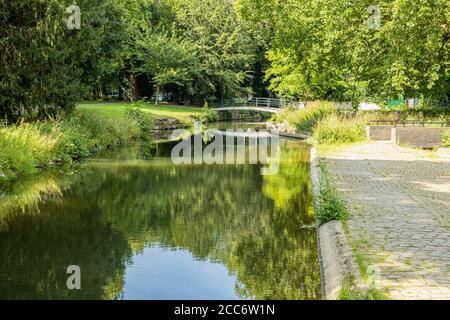 Bach mit Reflexion im Wasser umgeben von üppigen Bäumen Und eine kleine Fußgängerbrücke im Hintergrund in einem park in der Stadt Maastricht Stockfoto