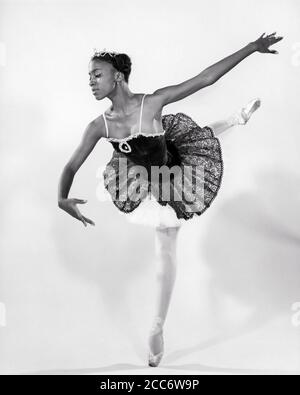 70ER JAHRE EINE AFROAMERIKANISCHE JUNGE LADY BALLERINA, DIE EINE ARABESKE HALTUNG AUFFÜHRT - D5954 HAR001 HARS INSPIRATION UNTERHALTUNG VERTRAUEN B & W PERFORMING PERFORMING KUNST TRÄUME GLÜCK WELLNESS PERFORMER AFRO-AMERIKANER AFROAMERIKANER HALTUNG KRAFTVOLLEN FORTSCHRITT TUTU SCHWARZ ETHNIZITÄT STOLZ BALLERINA ENTERTAINER BERUFE ARABESQUE KONZEPTIONELL STILVOLL KREATIVITÄT ENTERTAINER WACHSTUM PERFORMER JUNGE ERWACHSENE FRAU SCHWARZ UND WEISS ANMUTIGE HAR001 ALTMODISCH AUF PUNKT AFROAMERIKANER Stockfoto