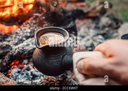 Kochender Kaffee in türkischer Cezva auf Lagerfeuer Kohlen. Luxus-Camping-Konzept. Stockfoto