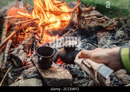 Luxus-Camping-Konzept. Frischer Kaffee in türkischer CEZVA auf Lagerfeuer Kohlen zubereitet. Stockfoto