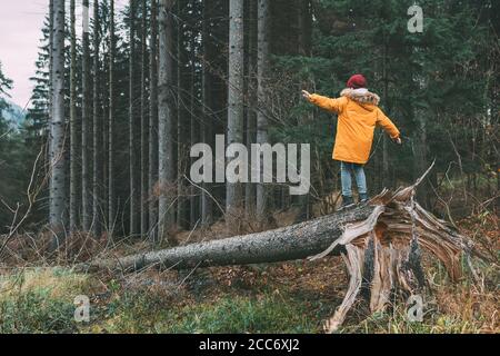 Junge in leuchtend gelben Parka (Kugeljacke) Spaziergänge im Pinienwald auf dem fallenden Baum Stockfoto