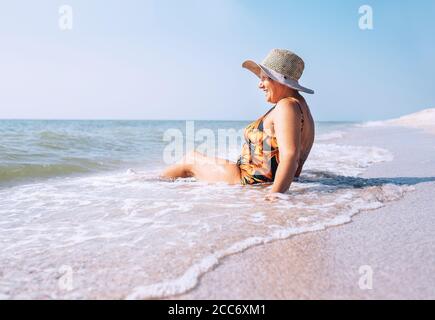 Ältere Frau genießen Strandurlaub sitzen auf dem Meer surfline Stockfoto
