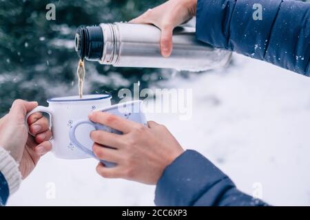 Hände mit Tassen Tee und Thermoskanne im Schnee Nahaufnahme des Winterwaldes Stockfoto