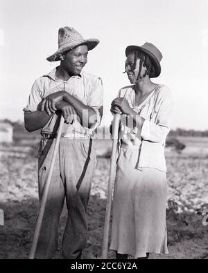 1930ER AFROAMERIKANISCHE EHEMANN FRAU, DIE EINANDER LÄCHELND ANSIEHT, HÖHLEND TABAK STÜTZT SICH AUF WERKZEUGE ZUSAMMEN NORTH CAROLINA USA - N67 HAR001 HARS SCHÖNHEIT WERKZEUGE GEMEINSCHAFT ANDERE JEDER AUSDRUCK ALTE ZEIT BESCHÄFTIGT NOSTALGIE LEHNTE INDUSTRIE ALTE MODE 1 GESICHTSKOMMUNIKATION JUNG ERWACHSENE BALANCE TEAMWORK STARK FREUDE FREUDE LIFESTYLE ZUFRIEDENHEIT FEIER FRAUEN VERHEIRATETE JOBS LÄNDLICHE EHEPARTNER EHEMÄNNER GESUNDHEIT VEREINIGTE STAATEN KOPIEREN RAUM FREUNDSCHAFT IN VOLLER LÄNGE IN HALBER LÄNGE DAMEN PERSONEN INSPIRATION VEREINIGTE STAATEN VON AMERIKA FÜRSORGLICHE LANDWIRTSCHAFT MÄNNER RISIKO GELASSENHEIT SPIRITUALITÄT VERTRAUEN AUSDRÜCKE LANDWIRTSCHAFT Stockfoto