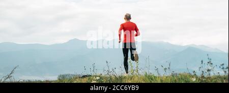 Weitwinkel-Shoot eines Mannes in roten Langarm-Shirt gekleidet läuft an der Straße mit Berg Hintergrund. Gesundes Lifestyle-Konzept. Stockfoto