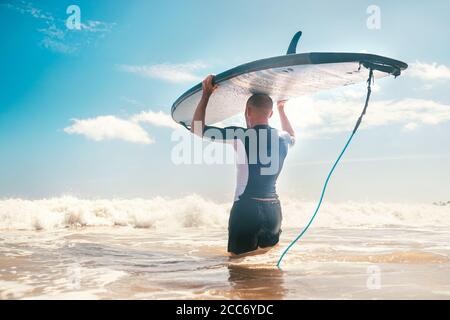 Young man Surfer mit langem Brett auf dem Kopf geht zum Meer, um eine Surf-Praxis zu haben. Surfkonzept lernen. Stockfoto