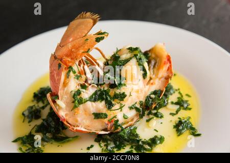 Ein halber Hummerschwanz, Homarus gammarus, der mit einer Butter, Knoblauch und Petersilie Sauce gegrillt und beträufelt wurde. Der Hummer wurde im Engli gefangen Stockfoto