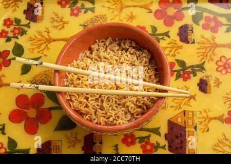 Eine Schüssel mit Instant-Nudeln auf einem farbenfrohen, malerischen Hintergrund. Bambusstäbchen werden auf die Schüssel gelegt. Stockfoto