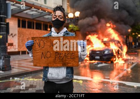 Seattle, USA, 30. Mai 2020: Ein Aktivist hält ein Zeichen NO JUSTICE NO PEACE, während ein Polizeiauto in Westlake im Hintergrund brennt. Stockfoto