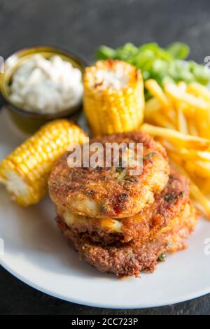 Drei Krabbenkuchen aus dem Fleisch einer braunen Krabbe, Cancer Pagurus, die im Ärmelkanal gefangen wurde. Serviert mit Knoblauch-Mayonnaise, Mais, Stockfoto