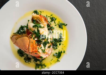 Ein halber Hummerschwanz, Homarus gammarus, der mit einer Butter, Knoblauch und Petersilie Sauce gegrillt und beträufelt wurde. Der Hummer wurde im Engli gefangen Stockfoto