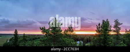 Luftpanorama der Mitternachtssonne über hellgrünem nordskandinavischen Wald - feuerbrennende Wolken, Tannenspitzen, kalte Sommernacht, gelbrote Spalte Stockfoto