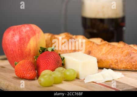 Gruyere Schweizer Käse, Becher Bier, Obst und Käsebrot auf einem Holzschneidebrett Stockfoto