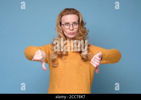 Düster unzufrieden reife Frau schaut auf Kamera zeigen Daumen nach unten. Stockfoto