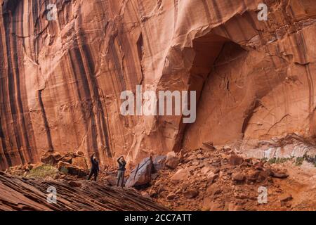 Mylène Jacquemart und Robert Hahn machen Fotos von hohen Sandsteinwänden im Stevens Canyon, in der Nähe des Escalante River, Utah. Stockfoto