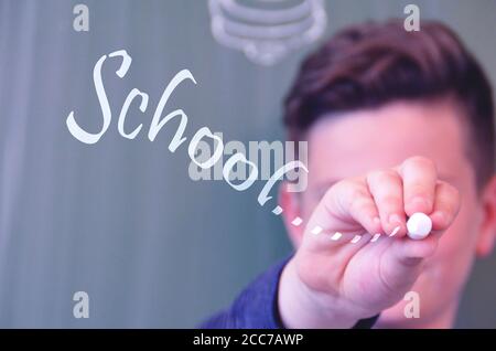 Der Schüler gibt das Wort "Schule" von Hand an das Glas des Fensters ein; Konzept für Schule und Bildung Stockfoto