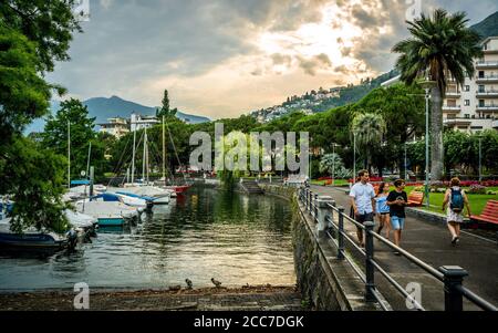 Locarno Schweiz , 1. Juli 2020 : Menschen auf Locarno Promenade am Ufer des Lago Maggiore bei Sonnenuntergang mit Blick auf den Yachthafen in Locarno Tessin Schweiz Stockfoto