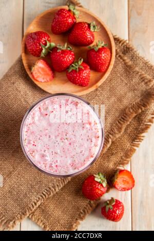 Frischer Milchshake mit Erdbeeren. Sommergetränk mit Beeren in einem Glas auf einem Holzhintergrund. Vertikales Foto Stockfoto