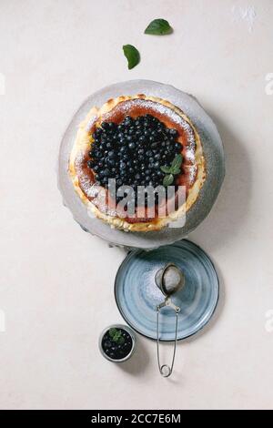 Ganze hausgemachte Heidelbeere gebacken weichen Käsekuchen san sebastian auf Keramik-Kuchen Stand Teller mit frischen Waldbeeren, Puderzucker und Minze über wh dekoriert Stockfoto