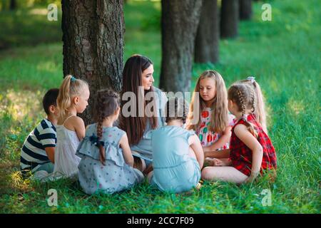 Kinder und Erziehung, junge Frau bei der Arbeit als Erzieher lesen Buch für Jungen und Mädchen im Park. Stockfoto
