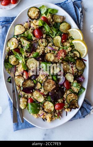 Zucchini Couscous Salat mit Kräutern, redd Zwiebel und Pflaumentomaten auf einem weißen ovalen Keramikplatte serviert. Stockfoto