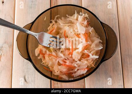 Hausgemachtes Sauerkraut mit Karotten in einer Glasplatte. Gemüse auf einem hellen Holzhintergrund einmachen. Öko-Lebensmittel, der Trend zu gesunder Ernährung. Stockfoto