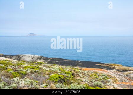 Granitfelsen entlang der Küste von Trousers Point, Flinders Island, Furneaux Group, Tasmanien, mit Mount Chappell Island in der Ferne. Stockfoto