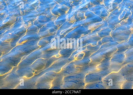 Sonnenbeschienenen Wellenflecken im flachen Wasser. Die hellen Wellen werden durch kleine Wellen gebeugt. Stockfoto