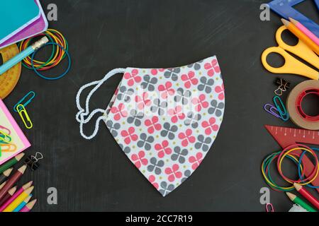 Draufsicht auf Schulbedarf und Stoffmaske auf Kreidetafel. Zurück zu den Schulrichtlinien während der covid-19 Pandemie Stockfoto