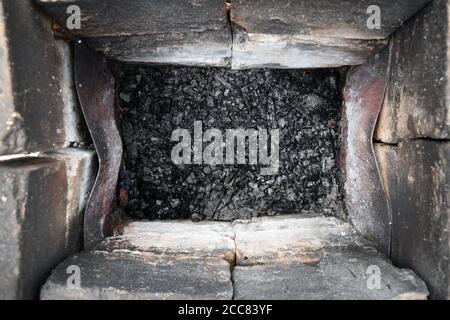 Blick von oben in den alten Kamin aus alten verbrannten Ziegeln, schmutzig mit Zunder. Schwarze Glut kühlt unten in mangal für Grill Stockfoto