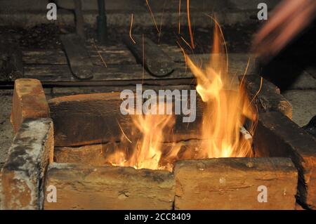 Unschärfe-Bewegung der Flammen über alten mangal aus verkohlten Terrakotta-Ziegeln. Lagerfeuer in Kohlebrazier mit dunklem Grunge Hintergrund Stockfoto