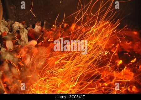 Funkenkohlenschnur fliegt vom Lagerfeuer. Helle Spuren von Flammenfunken. Brennende Spuren leuchten über schwarzem Hintergrund. Abstrakter feuriger Hintergrund Stockfoto