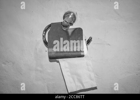 Dieses einzigartige Foto zeigt ein Schwarz-Weiß-Foto von Ein Toilettenpapierhalter aus Edelstahl befestigt an Eine weiße Steinmauer Stockfoto