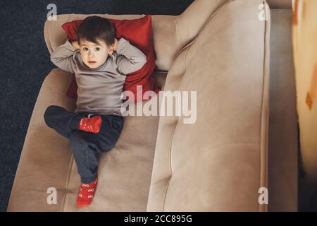 Oberes Porträt eines gelangweilten kaukasischen Jungen, der auf dem liegt Sofa mit einem roten Kissen, das zur Kamera aufschaut Stockfoto