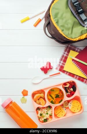 Lunchbox mit Gemüsesuppe, lustige Sandwiches in der Nähe der Schule Rucksack auf weißem Holz Hintergrund Stockfoto