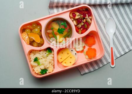 Lunchbox mit Gemüsesuppe, Salat und lustigen Sandwiches auf grauem Hintergrund Stockfoto