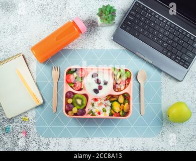 Lunchbox mit Reis, Gemüse und Obst, Beeren in yougurt auf Bürotisch neben Laptop Stockfoto