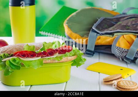 Lunchbox mit Sandwich in der Nähe von Keksen, Thermoskanne und Schulrucksack Stockfoto