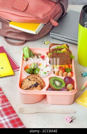 Lunchbox mit Sandwiches, Gemüsesalat und frischem Obst und Reis auf dem Tisch in der Nähe der Schule Rucksack Stockfoto