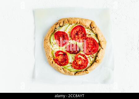 Eine Galette mit Ricotta-Käse, Zucchini und Tomaten, weißem Backpapier, weißem Hintergrund, Draufsicht Stockfoto