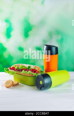 Farbe Thermoskrüge neben Lunchbox über hellgrün Bokeh Hintergrund Stockfoto