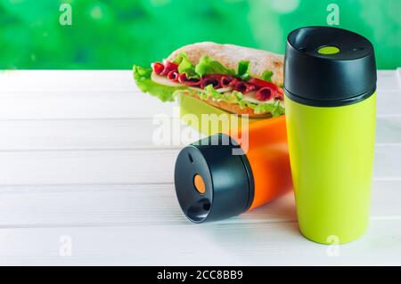 Farbe Thermoskanne Tassen neben Lunchbox auf weißem Holztisch Stockfoto