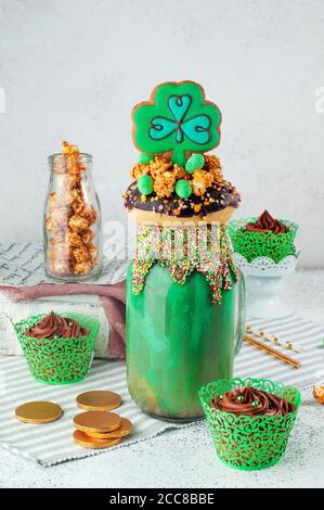 St. Patrick's Freak Shake Topping mit Kleeblätzchen und Schokolade Cupcakes auf grauem Hintergrund Stockfoto