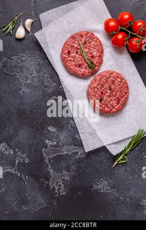 Frisches rohes Fleisch-Burger-Cutlet mit Kräutern und Gewürzen auf der schwarzen Steinplatte, Draufsicht Stockfoto