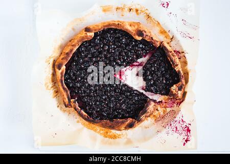 Eine schwarze Johannisbeergalette auf Backpapier auf weißem Hintergrund, eine Scheibe mit einem abgebissenen Stück, Draufsicht Stockfoto