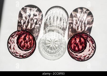 Kristall rotes Glas auf weißem Tisch. Harte Schatten im Sonnenlicht. Stockfoto