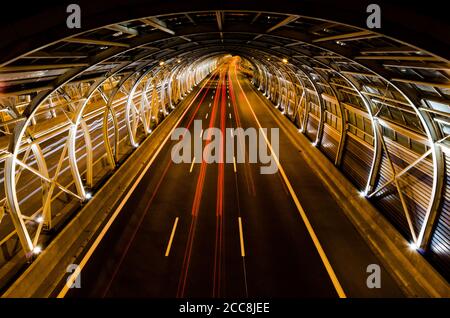 Mehrzeiliger, erdgestützter Glastunnel auf der Autobahn. Geschwindigkeitslinien von Autos in Bewegung in einem modernen, auf Glas-Tunnel von der Nacht fotografiert basiert. Stockfoto