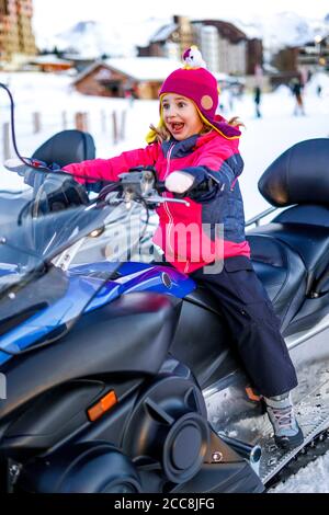 Funny Girl sitzt auf einem Quad im Winter in den französischen Alpen. Geländefahrzeug in Bewegung im Winter. Stockfoto