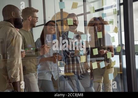 Junge multirassische Business-Team, Gruppe von kreativen Menschen Blick auf Haftnotizen auf Glas-Board und diskutieren etwas, arbeiten zusammen in modernen Stockfoto